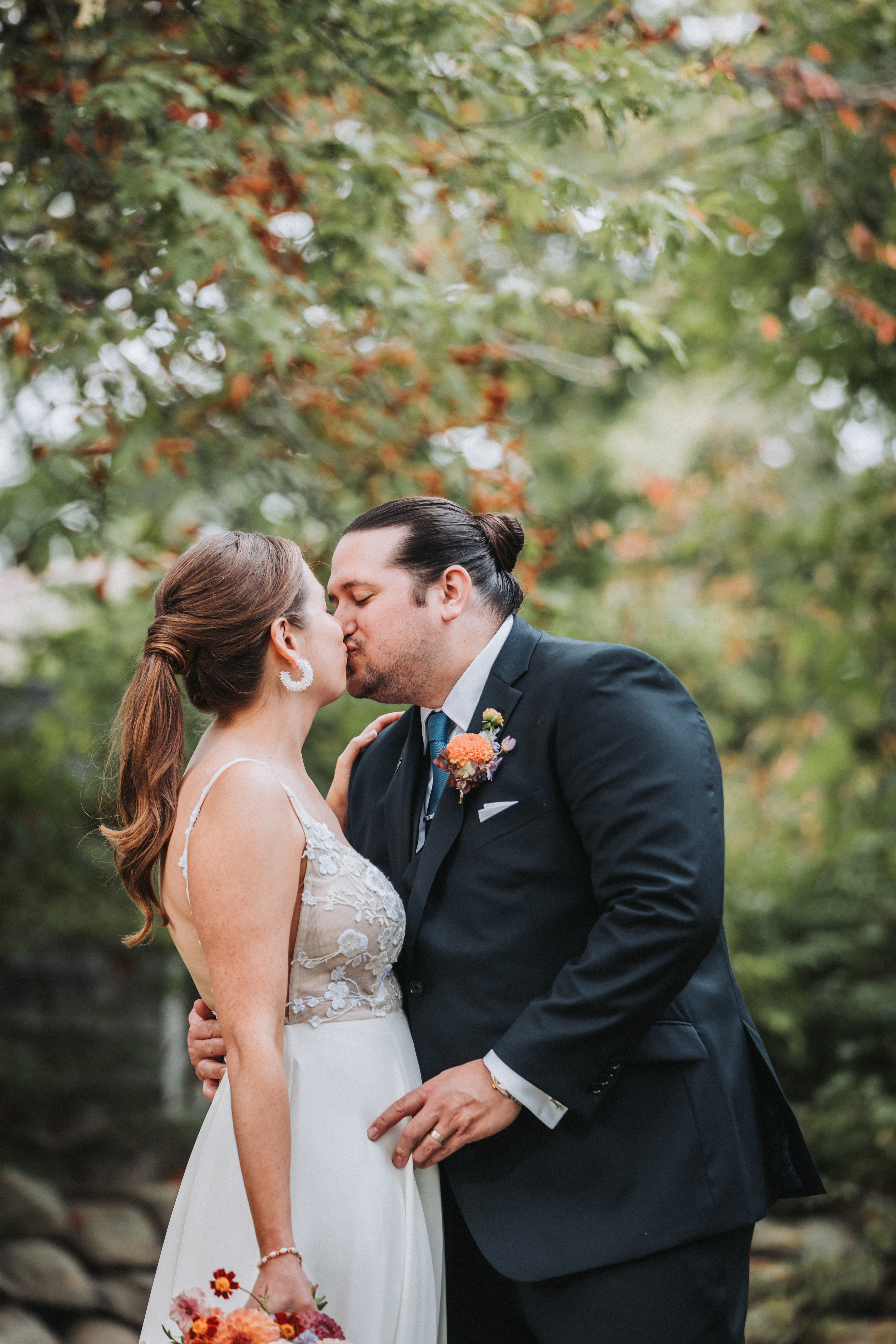 Newlyweds kissing beneath a tree turning orange, warm autumn light through the leaves behind them
