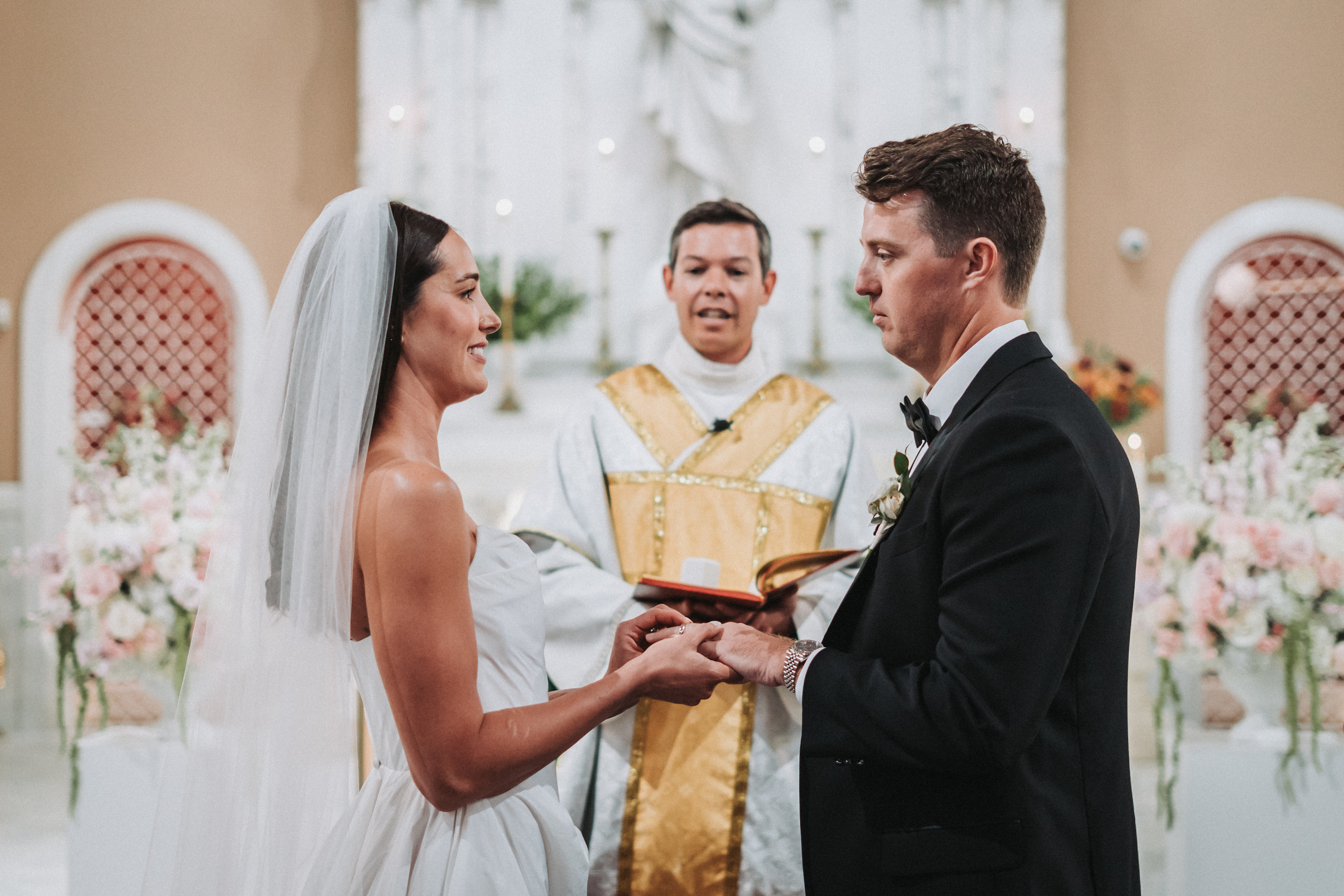 Bride and groom exchanging rings at the altar as their officiant reads from the ceremony book