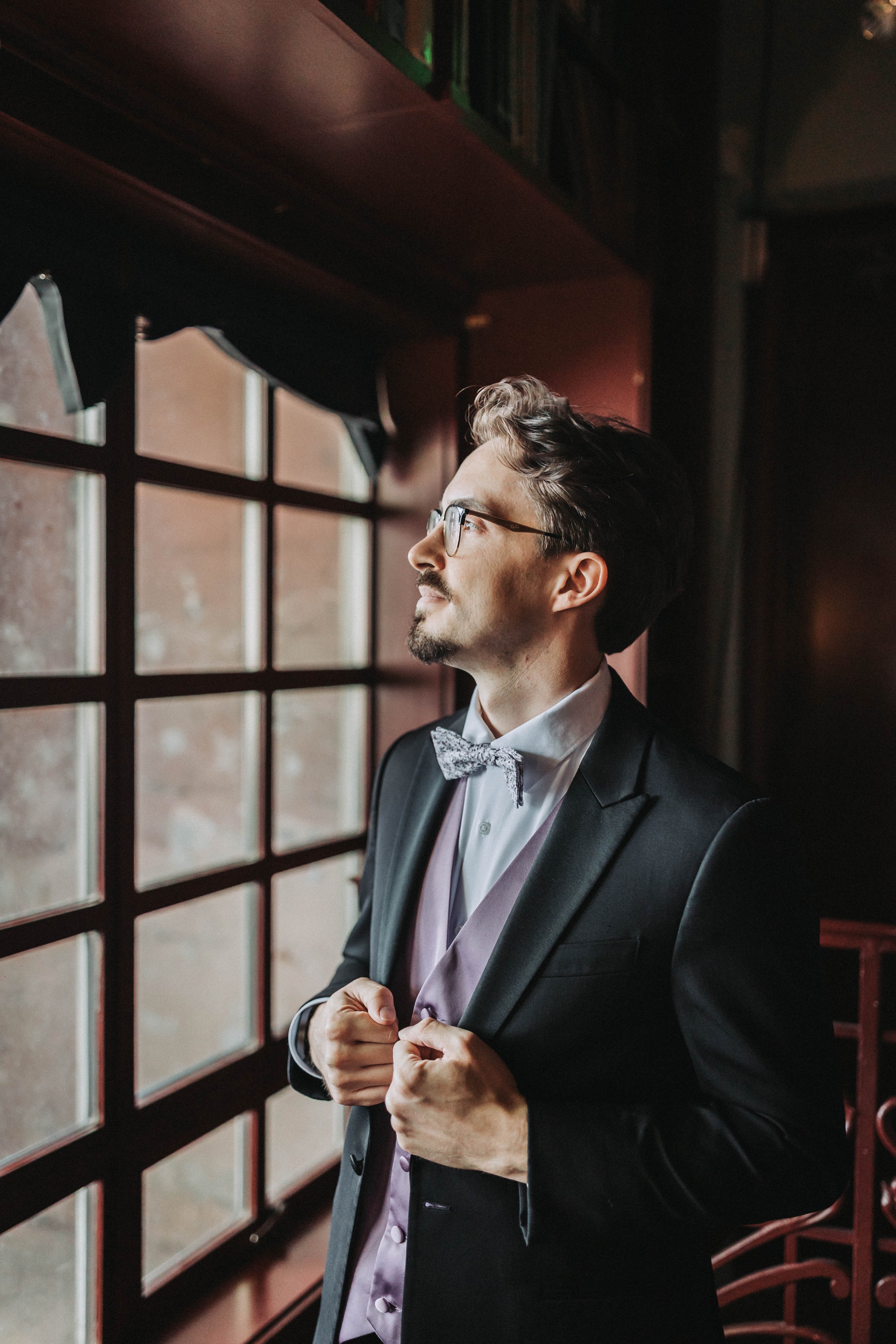 Groom fastening his jacket by a tall window before the ceremony — Seattle, Washington wedding photography