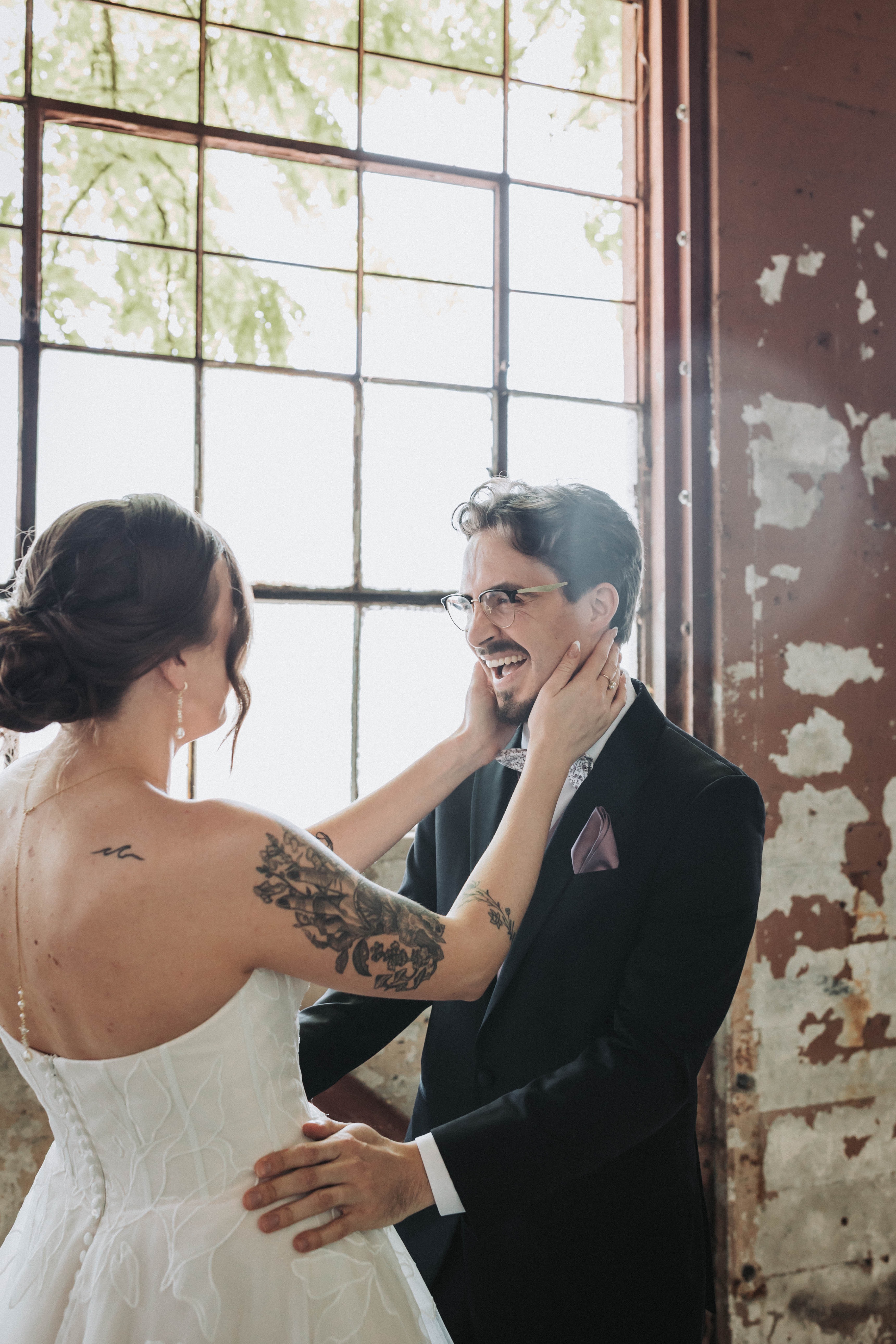 Bride cupping the groom's face at their first look, beside an industrial window — Seattle, Washington wedding photography