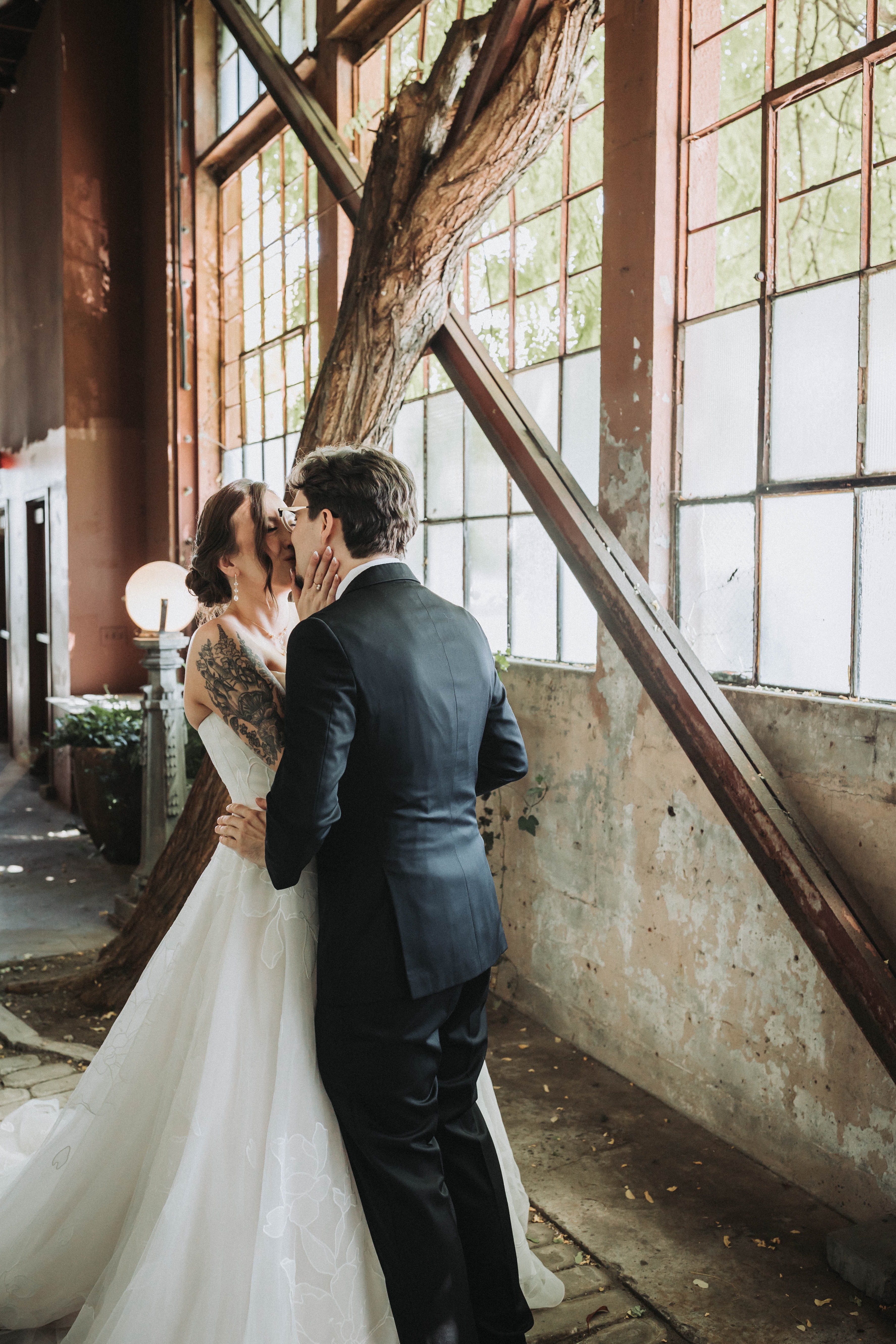 Couple kissing in the light of a tall factory window at their first look — Seattle, Washington wedding photography