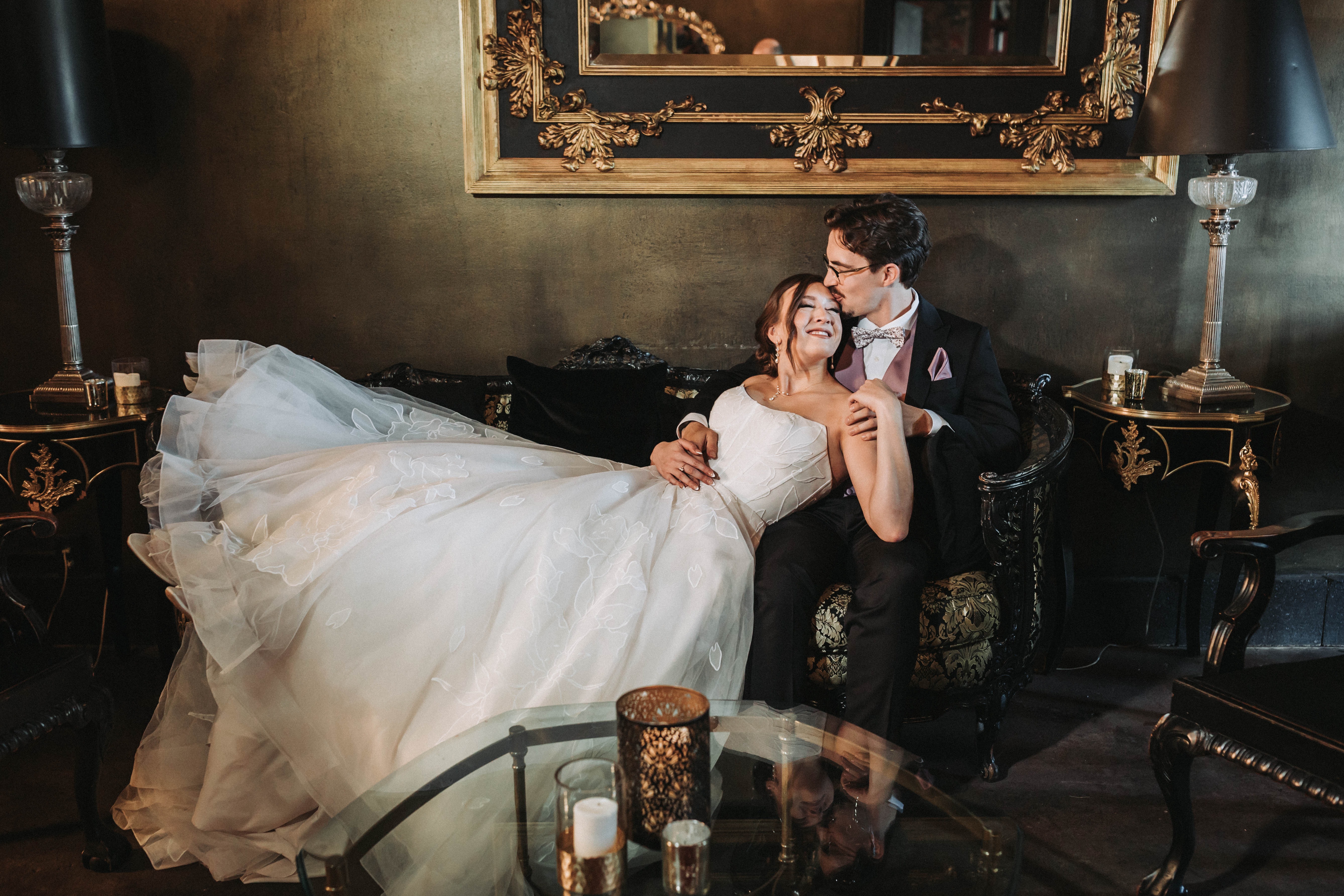 Couple resting together on an antique sofa in candlelight, the bride's train spread across the floor — Seattle, Washington wedding photography