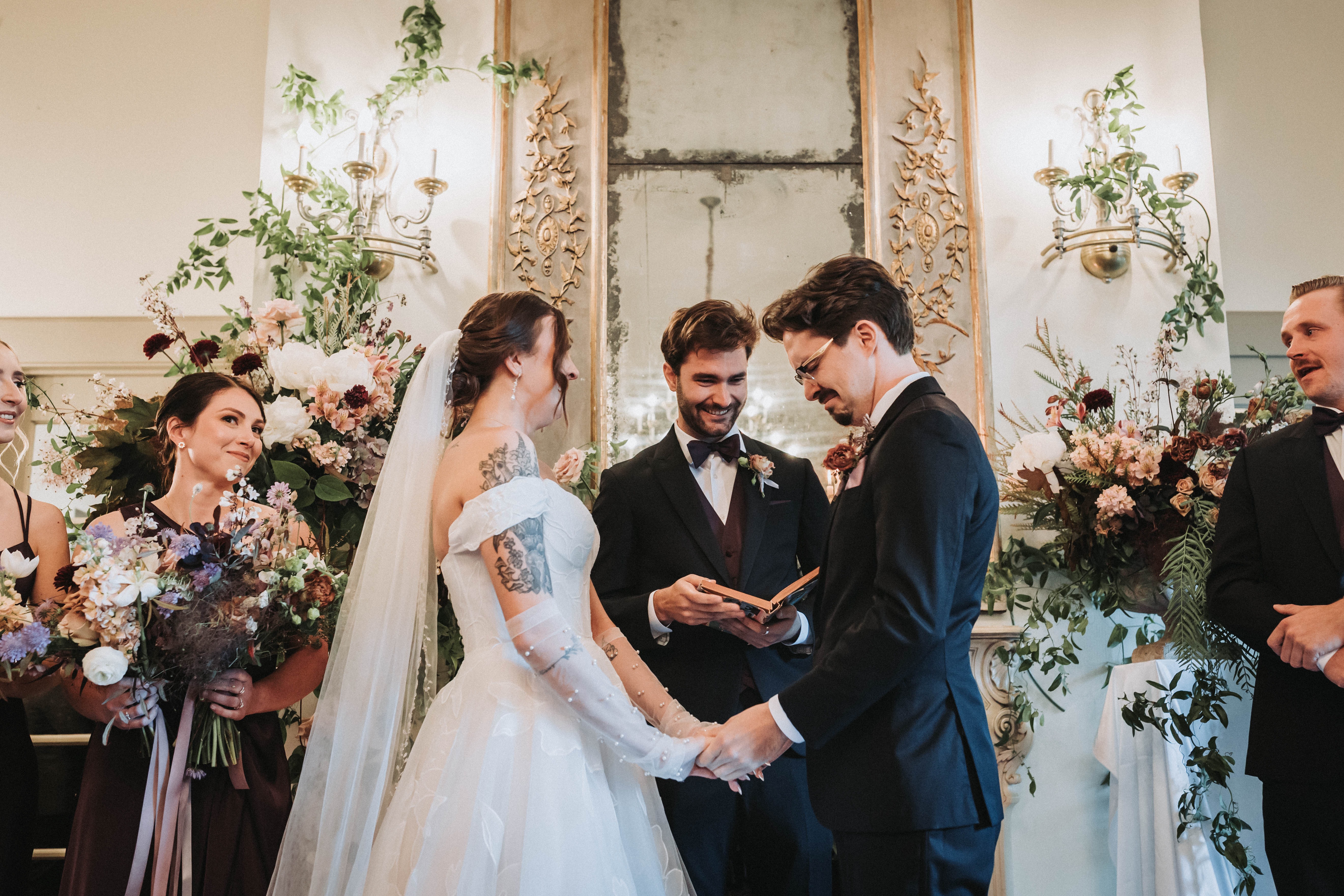Couple holding hands through their vows in front of their wedding party and tall floral arrangements — Seattle, Washington wedding photography