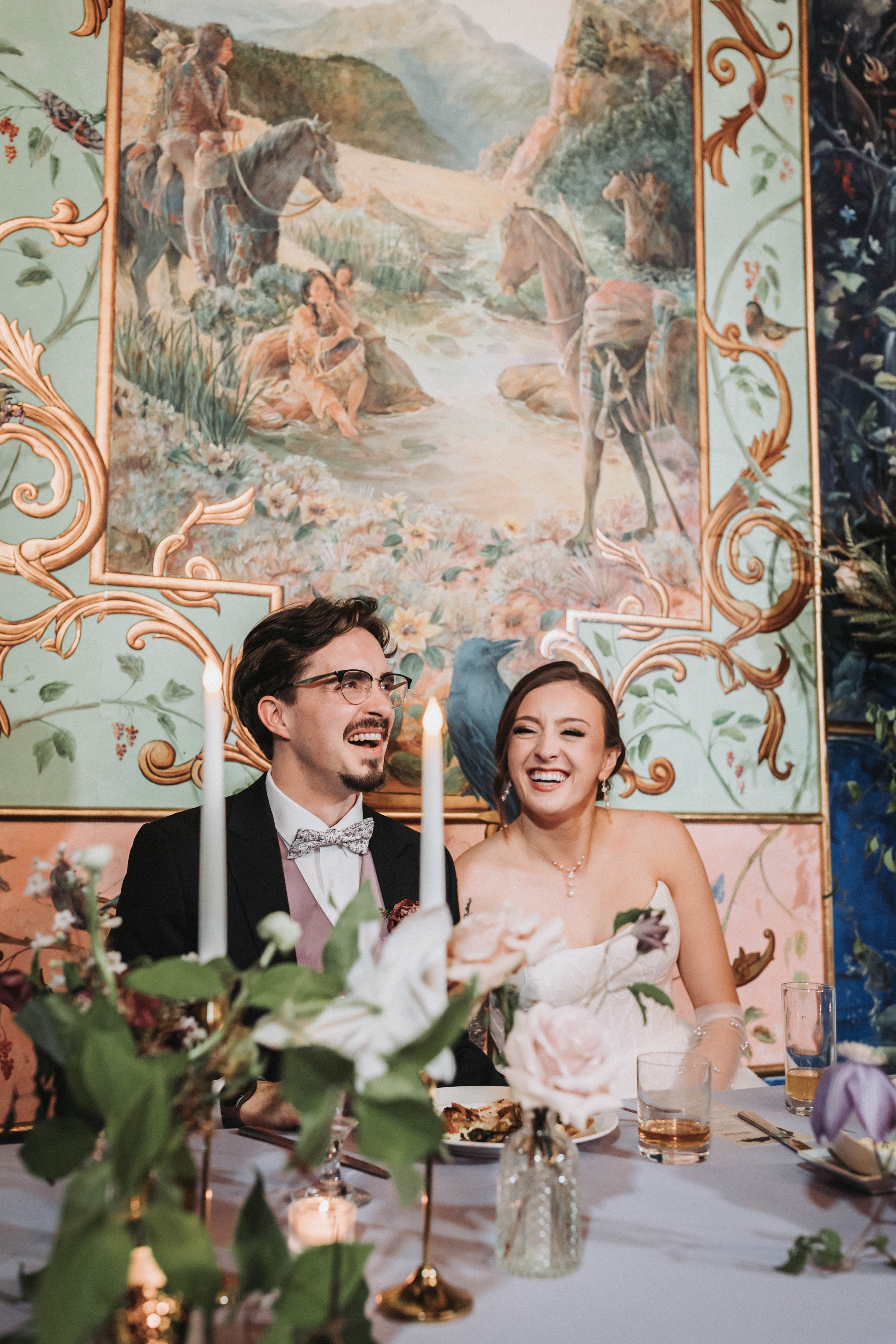 Couple laughing together at the head table beneath a painted mural at the reception — Seattle, Washington wedding photography